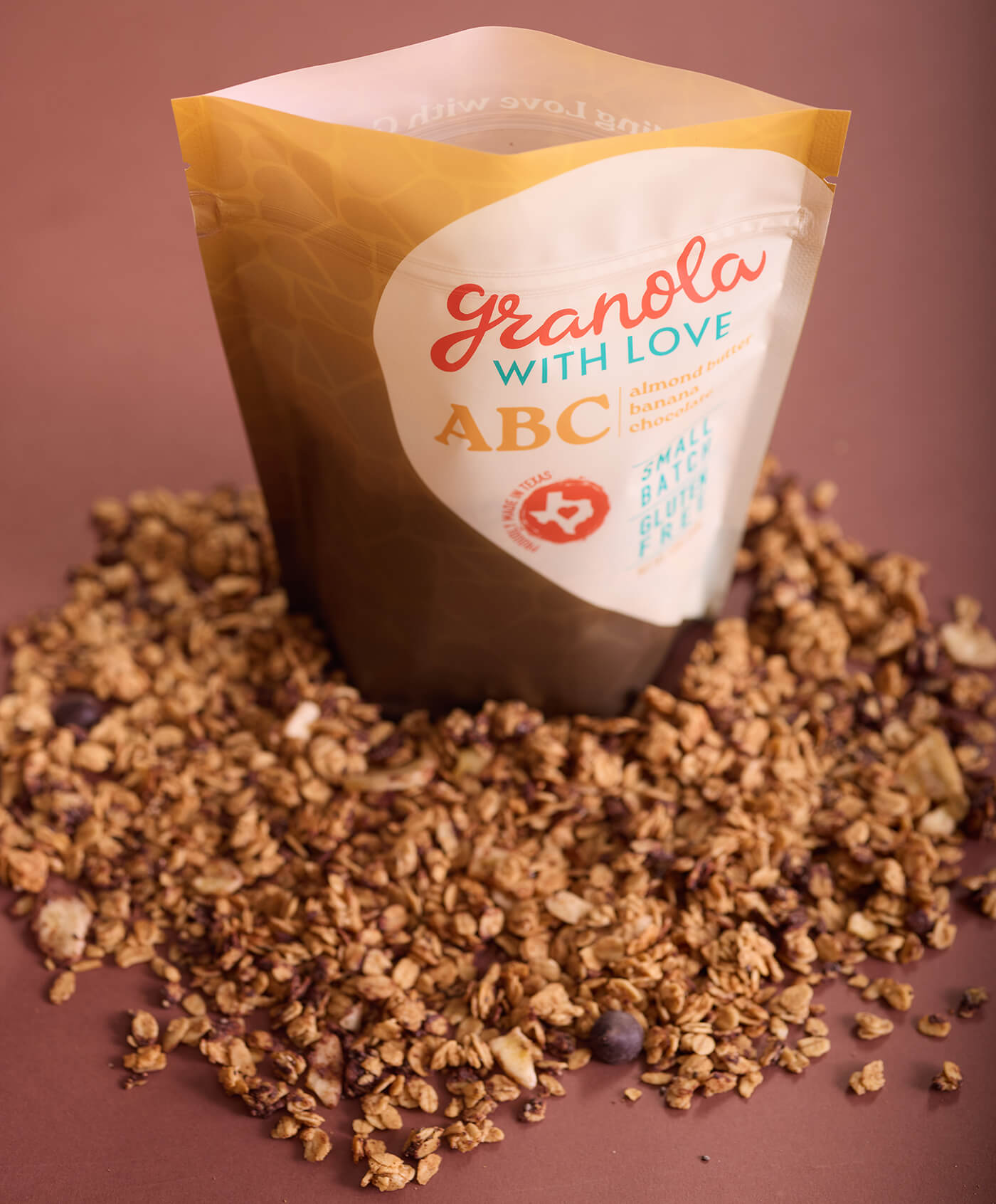 Granola with Love ABC packaging surrounded by granola on a brown background
