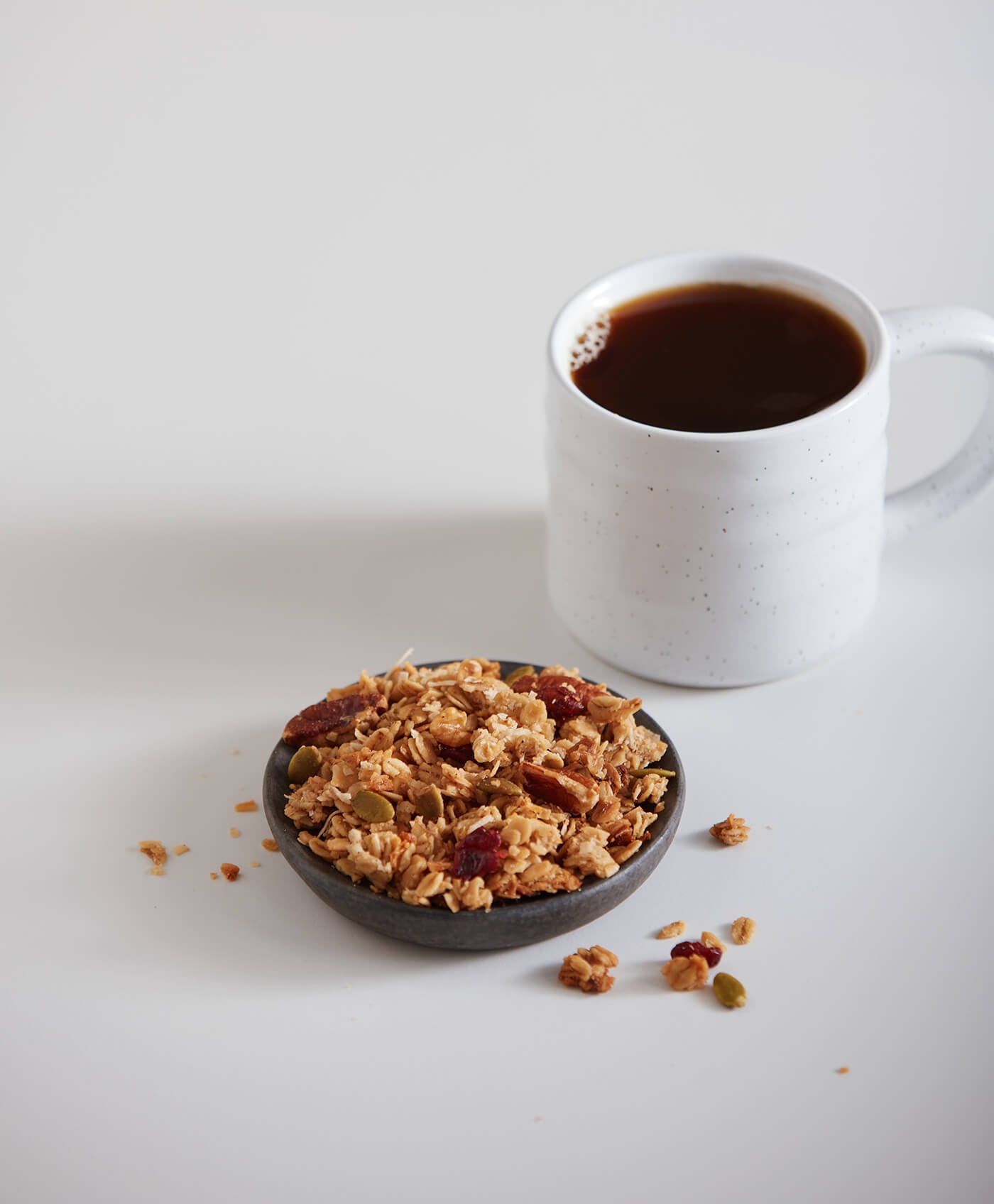 Bowl of granola with a mug of coffee on a white surface